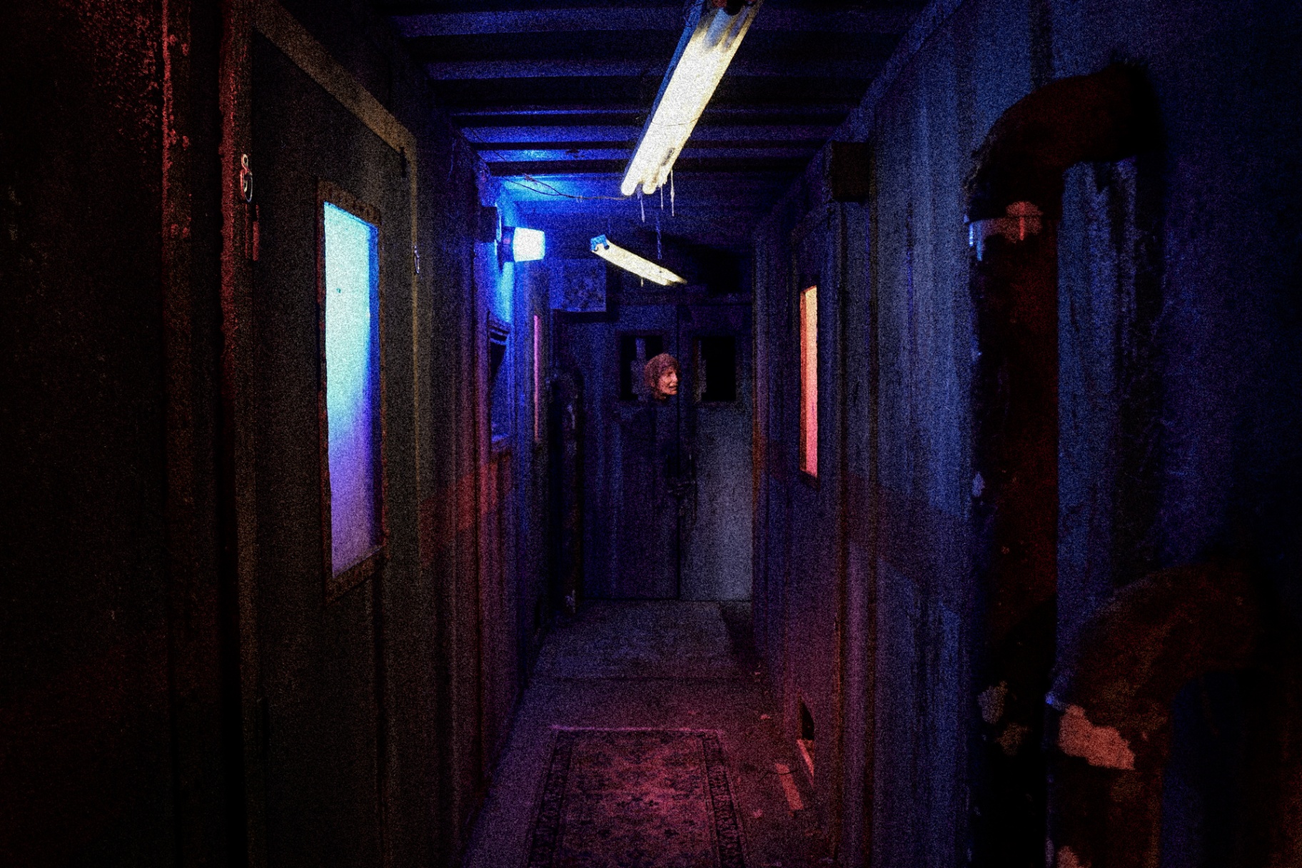 Dark hallway lit blue and red with figure at the end